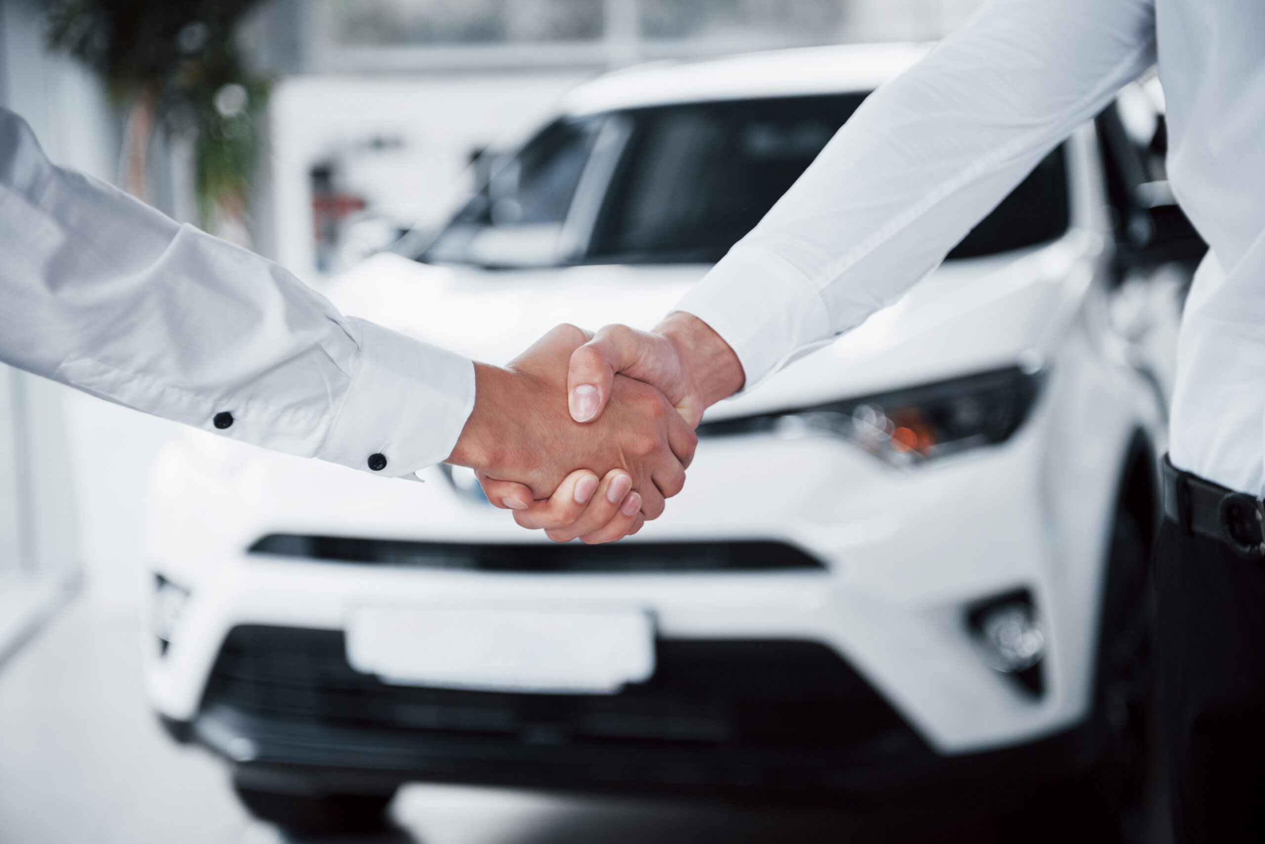 Two people shaking hands in a dealership office, symbolizing a successful dealership warranty sales agreement.