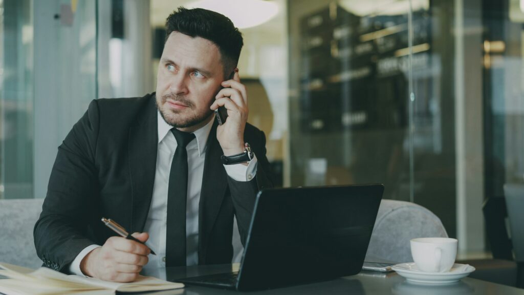 Man in a suit talking on the phone at a desk with a laptop