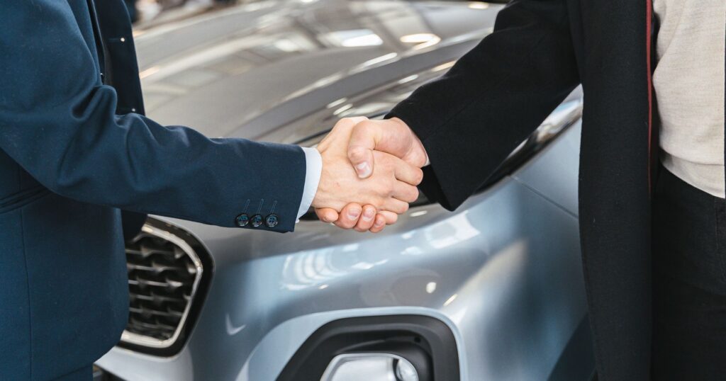 Two people shaking hands in front of a car in a dealership showroom