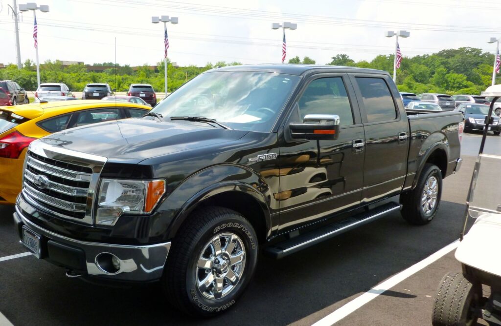 Black pickup truck parked in a row on a sunny car dealership lot